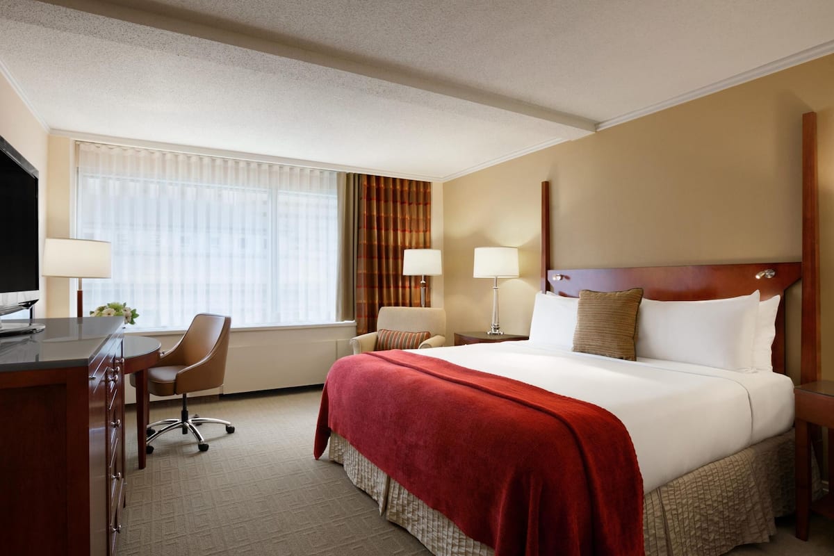 A hotel room with a large bed, a desk with a chair, two bedside lamps, and a television.
