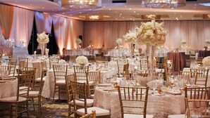 A banquet hall with round tables, gold chairs, and white tablecloths.