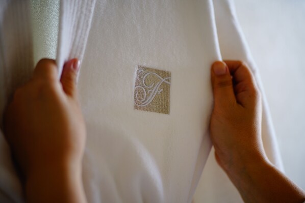A hand holding a white garment with a square embroidered logo.