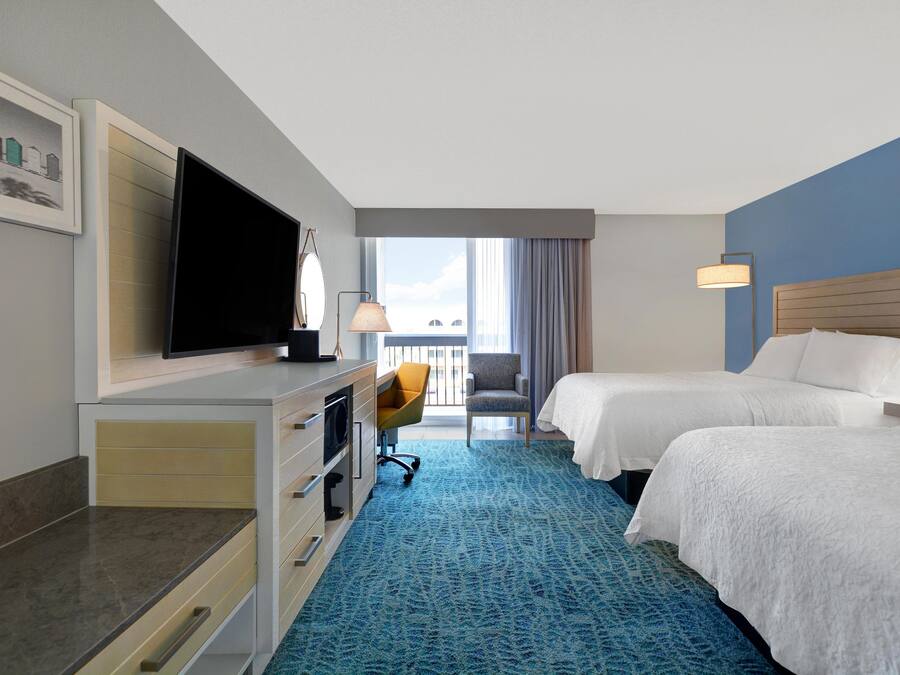 A hotel room with a bed, a desk with a television, a chair, and a view of the outside.