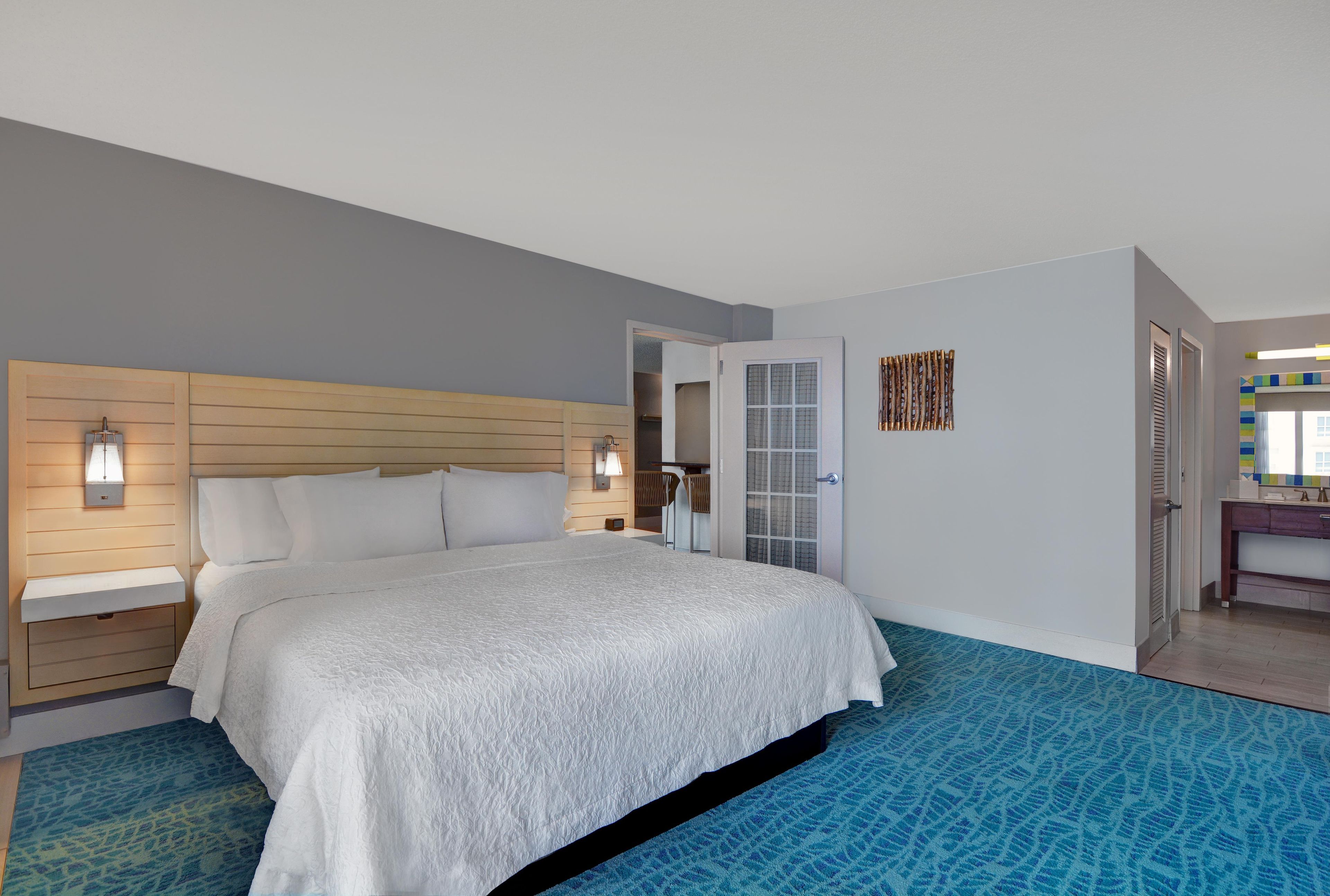 A hotel room with a bed, bedside lamps, a door, and a bathroom visible through an open door.