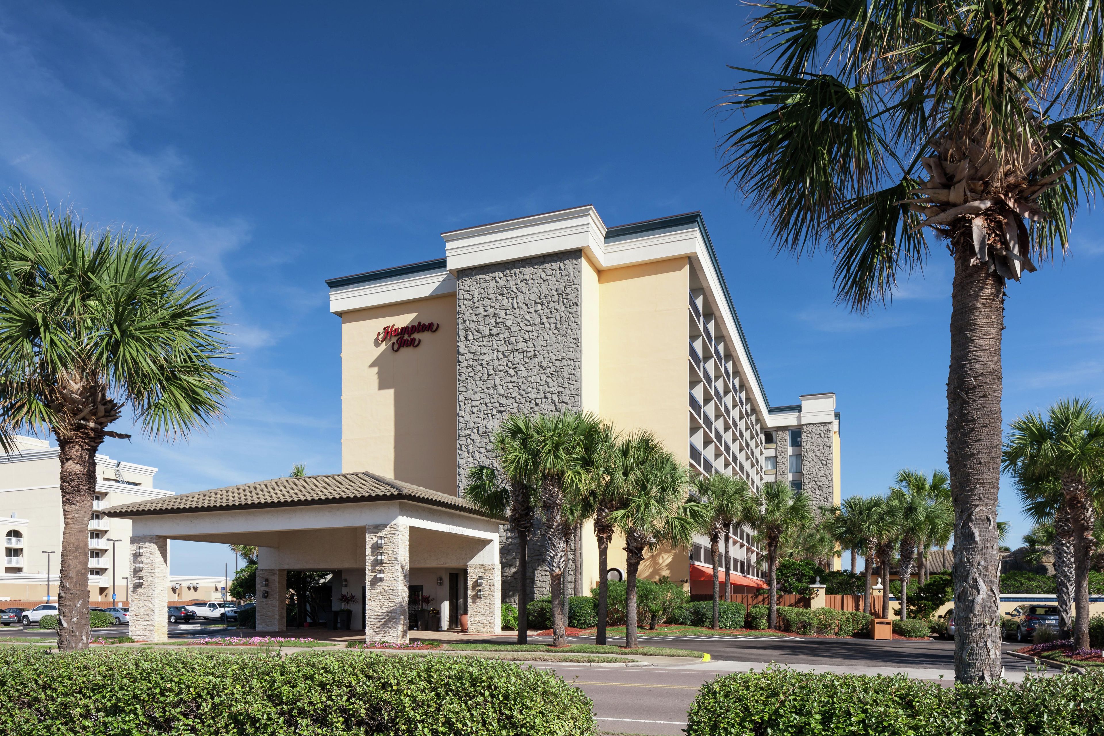 A hotel with a stone facade, palm trees, and a clear blue sky.