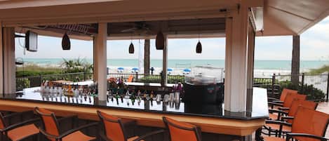 Un bar junto a la playa con una barra larga, varias sillas y vista al océano.