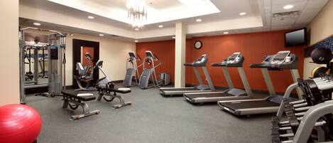 A gym with treadmills, elliptical machines, a weight bench, and a red exercise ball.