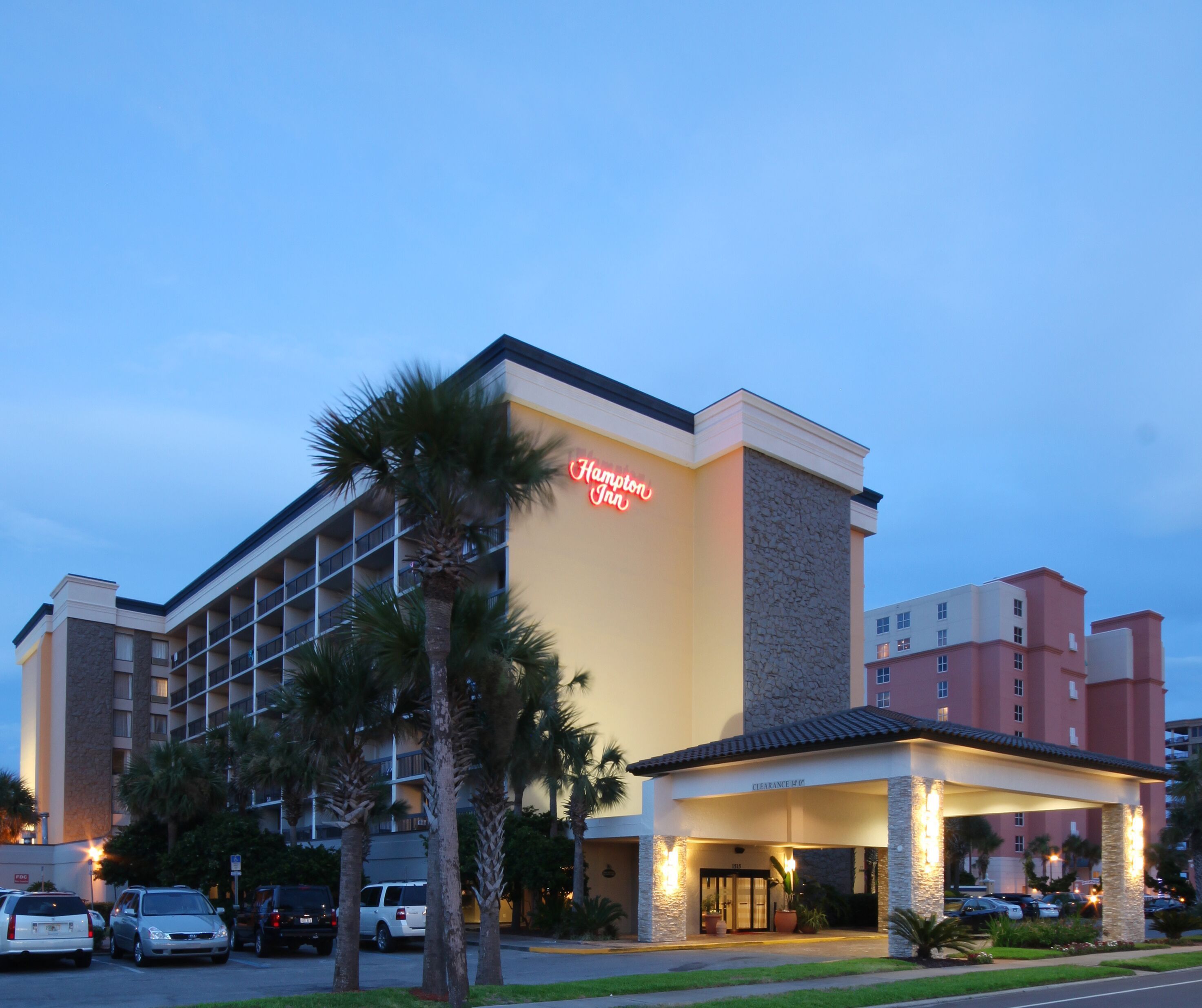 A hotel with a stone facade, a neon sign, and a covered entrance.