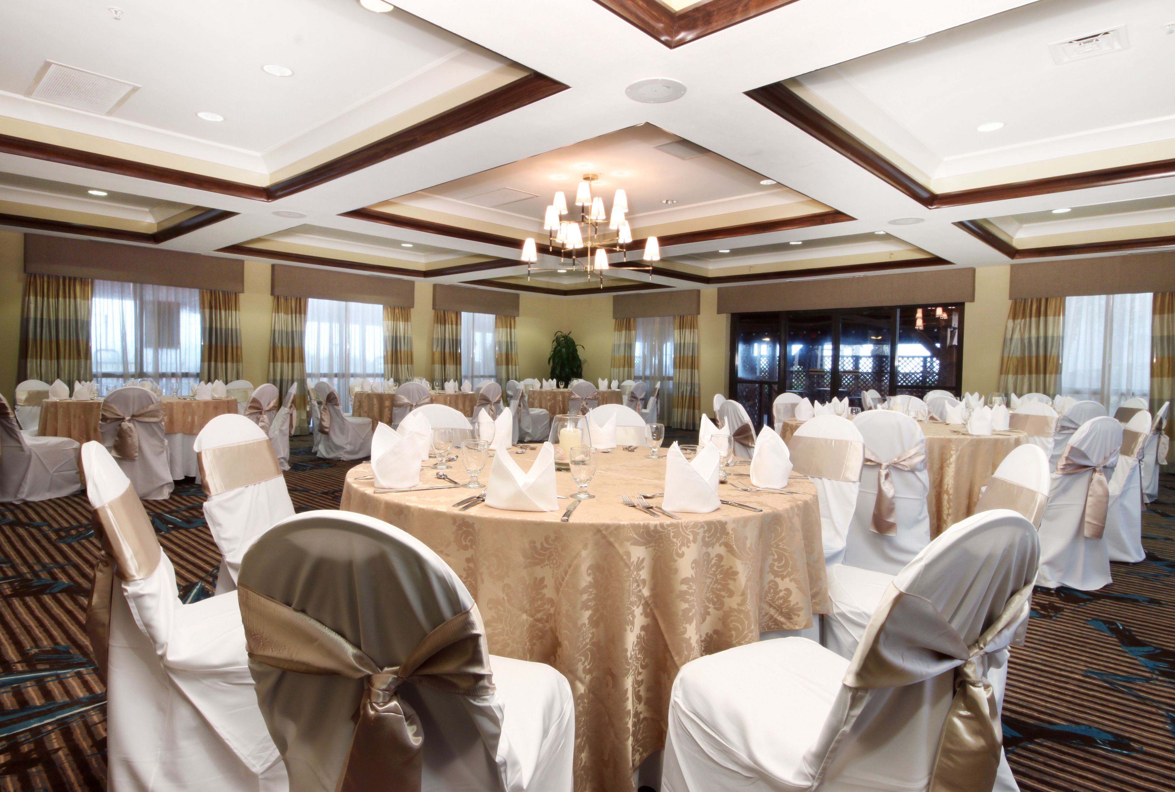 A banquet hall with round tables, white chairs, and chandeliers.
