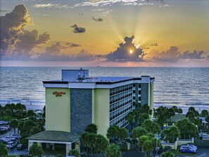 A hotel with a view of the ocean at sunset, featuring a parking lot and palm trees. - Hampton Inn Jacksonville Beach/Oceanfront (Jacksonville Beach)