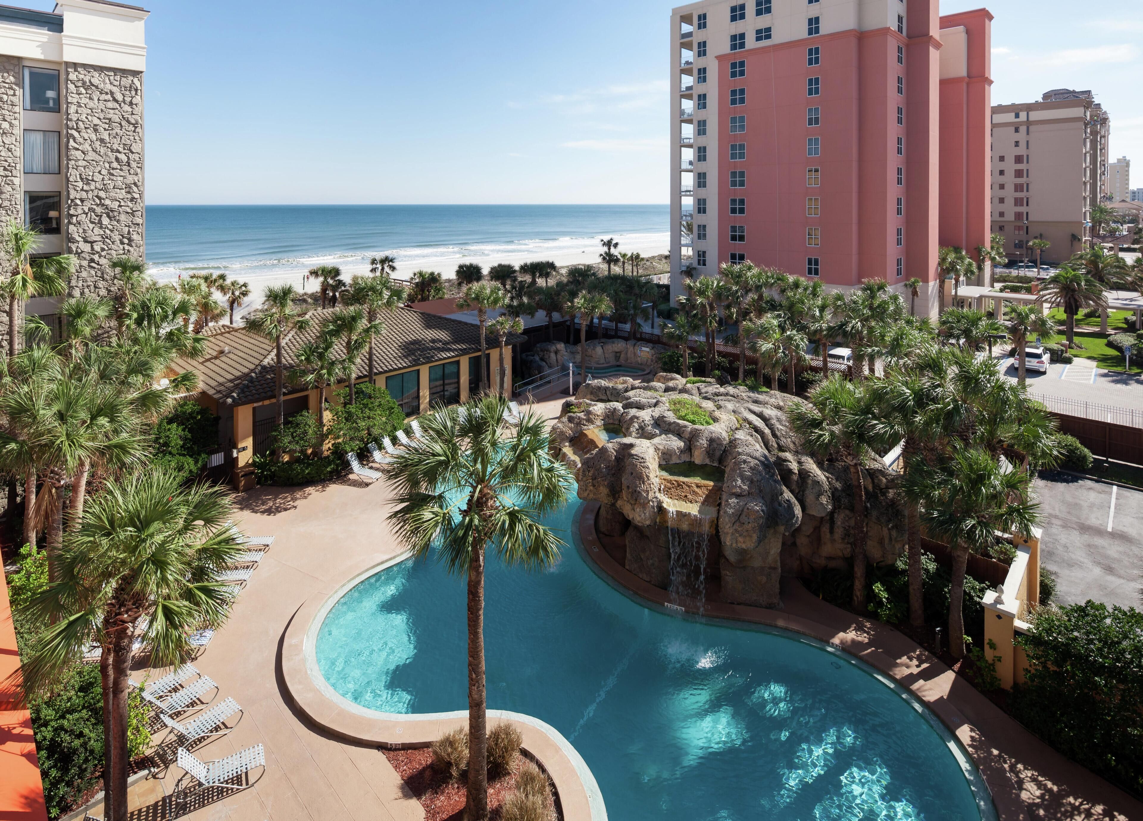 Un resort con piscina, palmeras y vista a la playa.