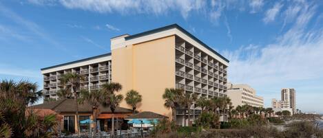 A hotel with multiple floors, outdoor seating, and palm trees.