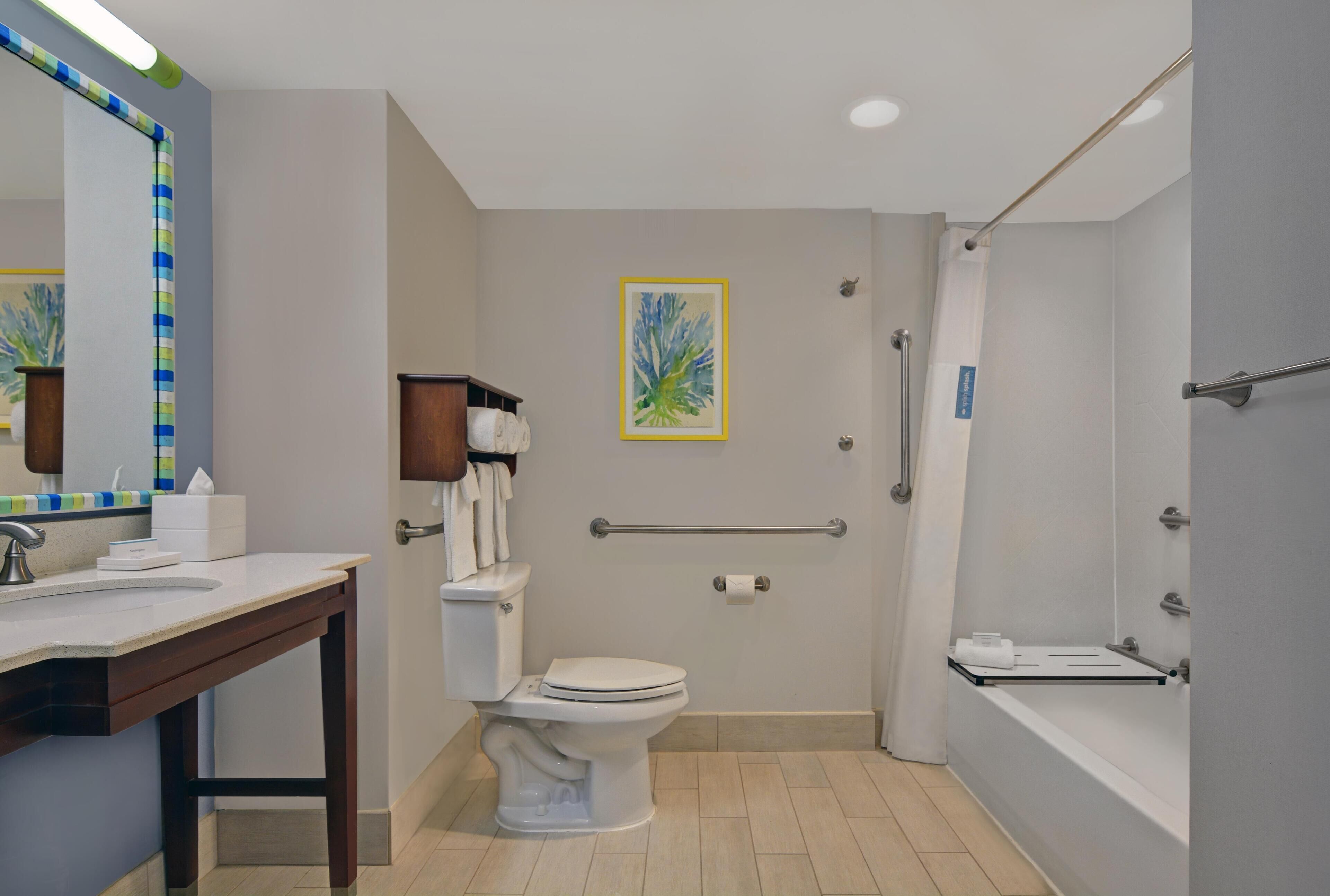 Baño con inodoro, lavamanos, ducha y barra de apoyo.