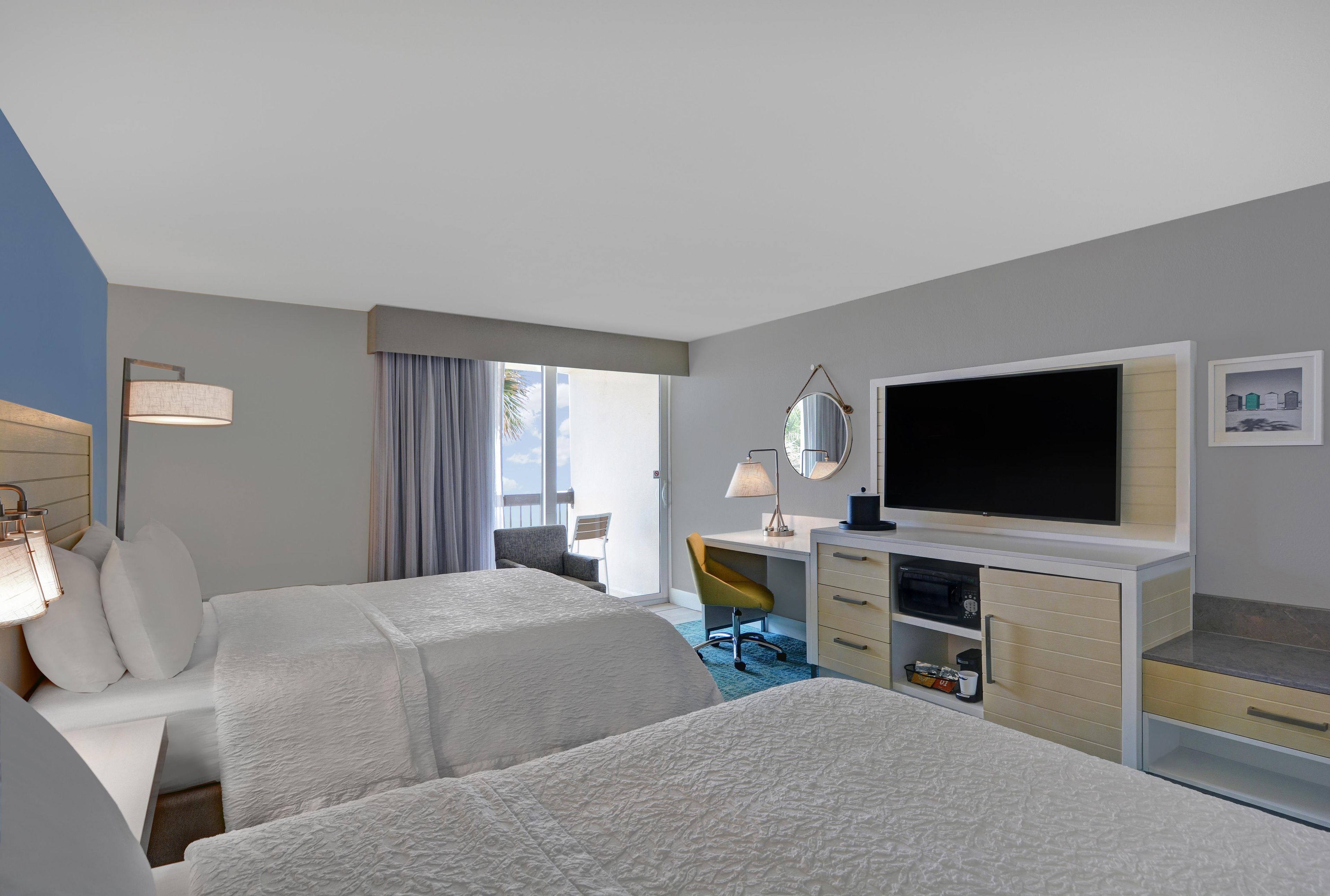 A hotel room with two beds, a desk, a television, and a window with curtains.