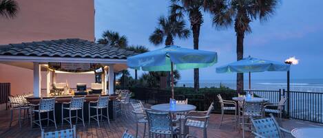 A deck with outdoor seating, a bar area, and a view of the ocean.
