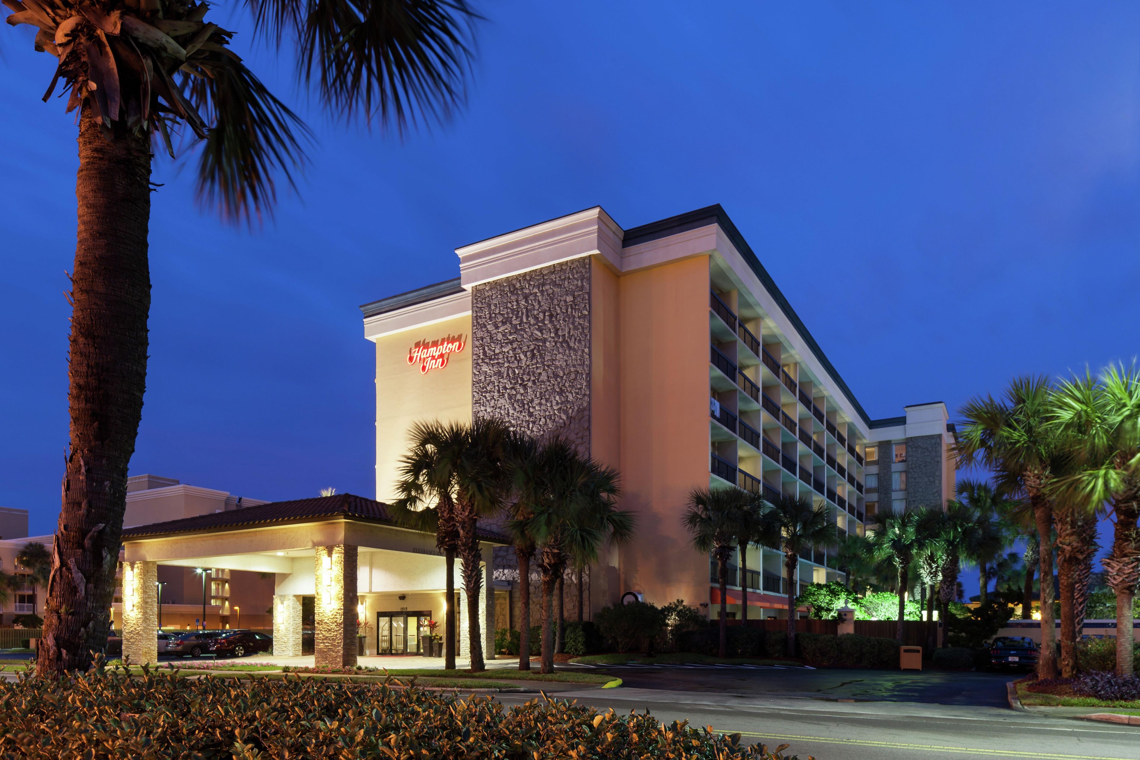 Een hotel met een herkenbaar Hampton Inn bord, een overdekte ingang en palmbomen.