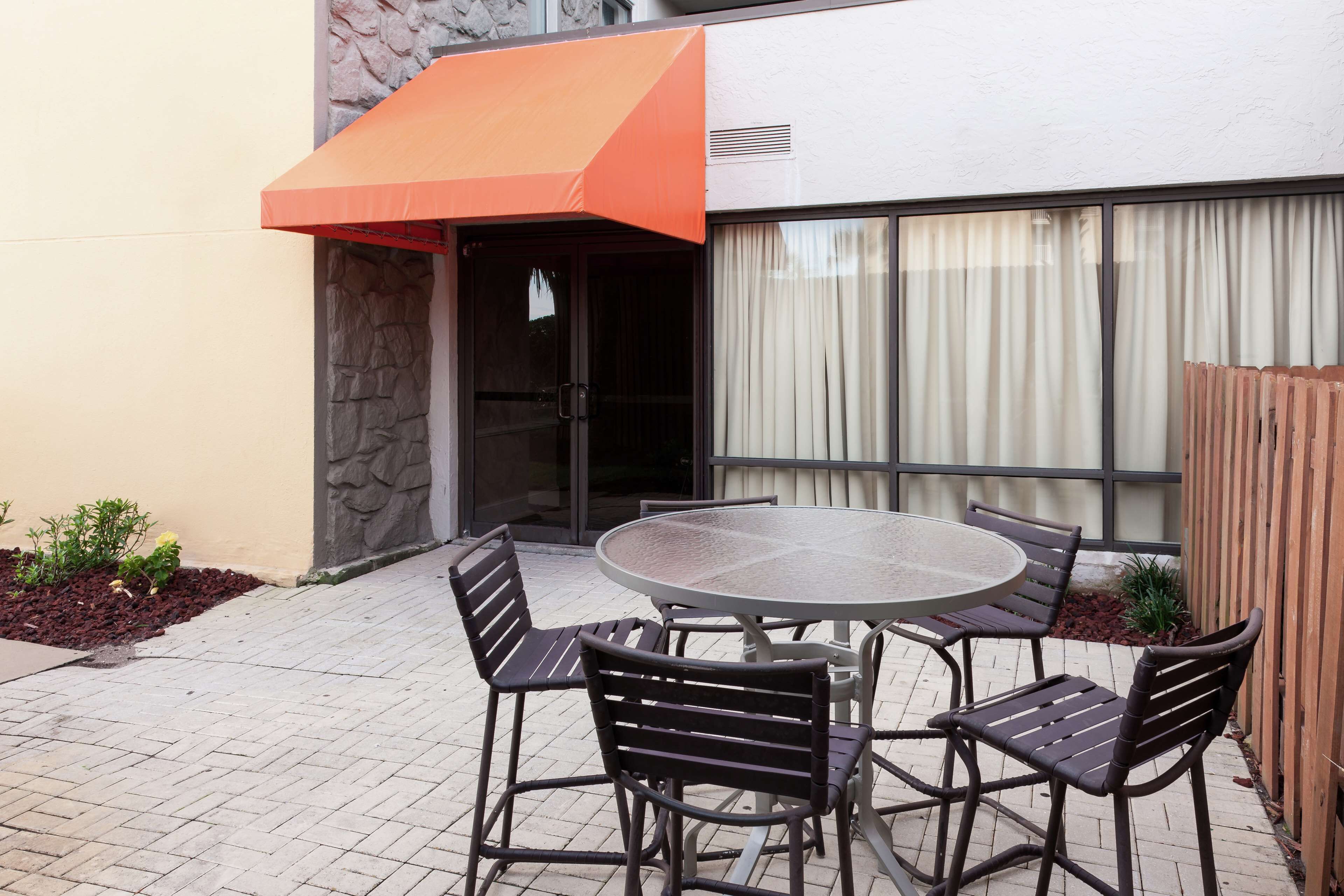 An outdoor patio with a round table and four chairs, a stone wall, and a wooden fence.