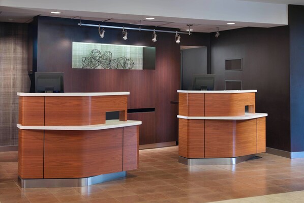 A reception area with two wooden reception desks, a modern wall art piece, and a large mirror.