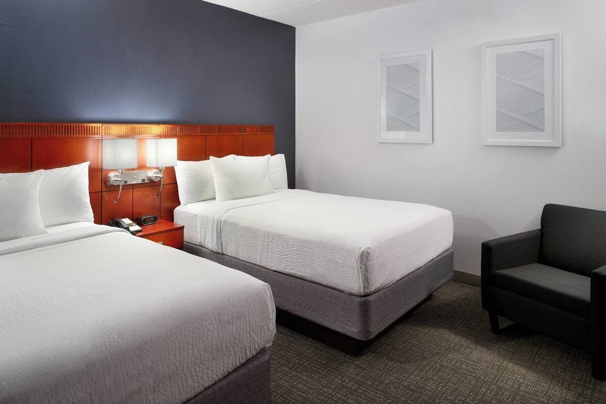 A hotel room with two beds, a nightstand with a phone, a chair, and two wall-mounted picture frames.
