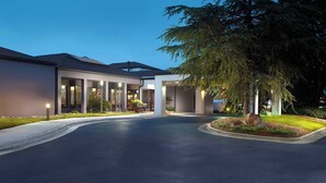 A modern building with a curved driveway, large windows, and a well-lit entrance area. - Courtyard by Marriott Raleigh Midtown (Raleigh)