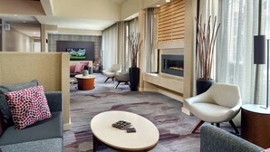 A modern hotel room with a cozy seating area, a fireplace, and a television in the background. - Courtyard by Marriott Raleigh Midtown (Raleigh)