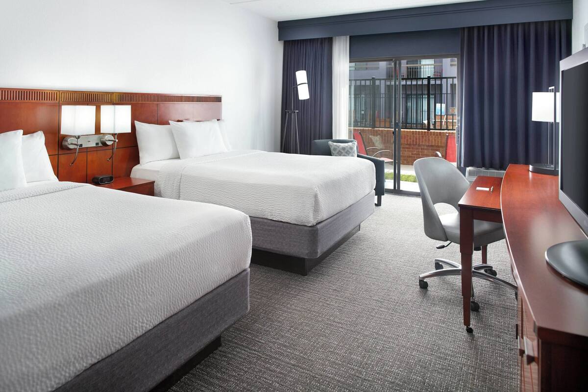A hotel room with two beds, a desk, a chair, and a TV.