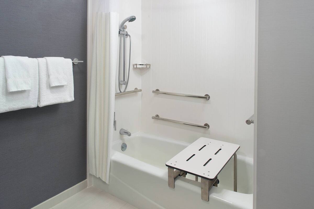 A bathroom with a bathtub, grab bars, and a small step stool for accessibility.
