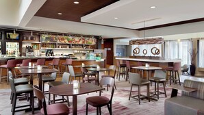 A modern hotel lobby with a bar area, seating arrangements, and a coffee station. - Courtyard by Marriott Raleigh Midtown (Raleigh)