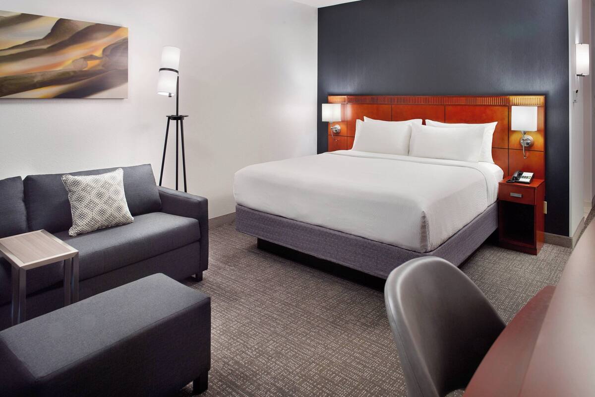 A hotel room with a bed, a sofa, a desk, and a chair.