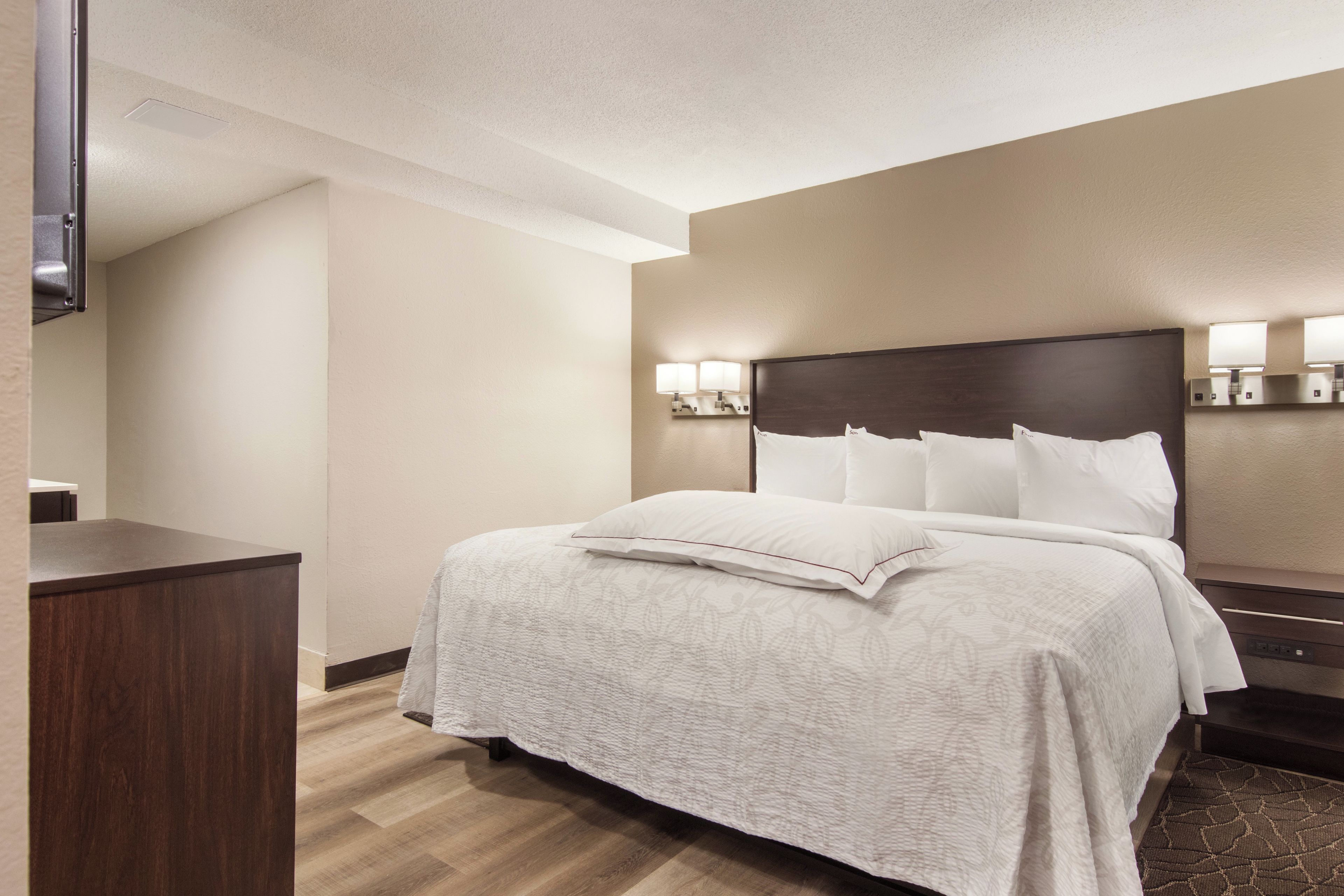 A hotel room with a bed, bedside tables, a desk, and a wall-mounted lamp.