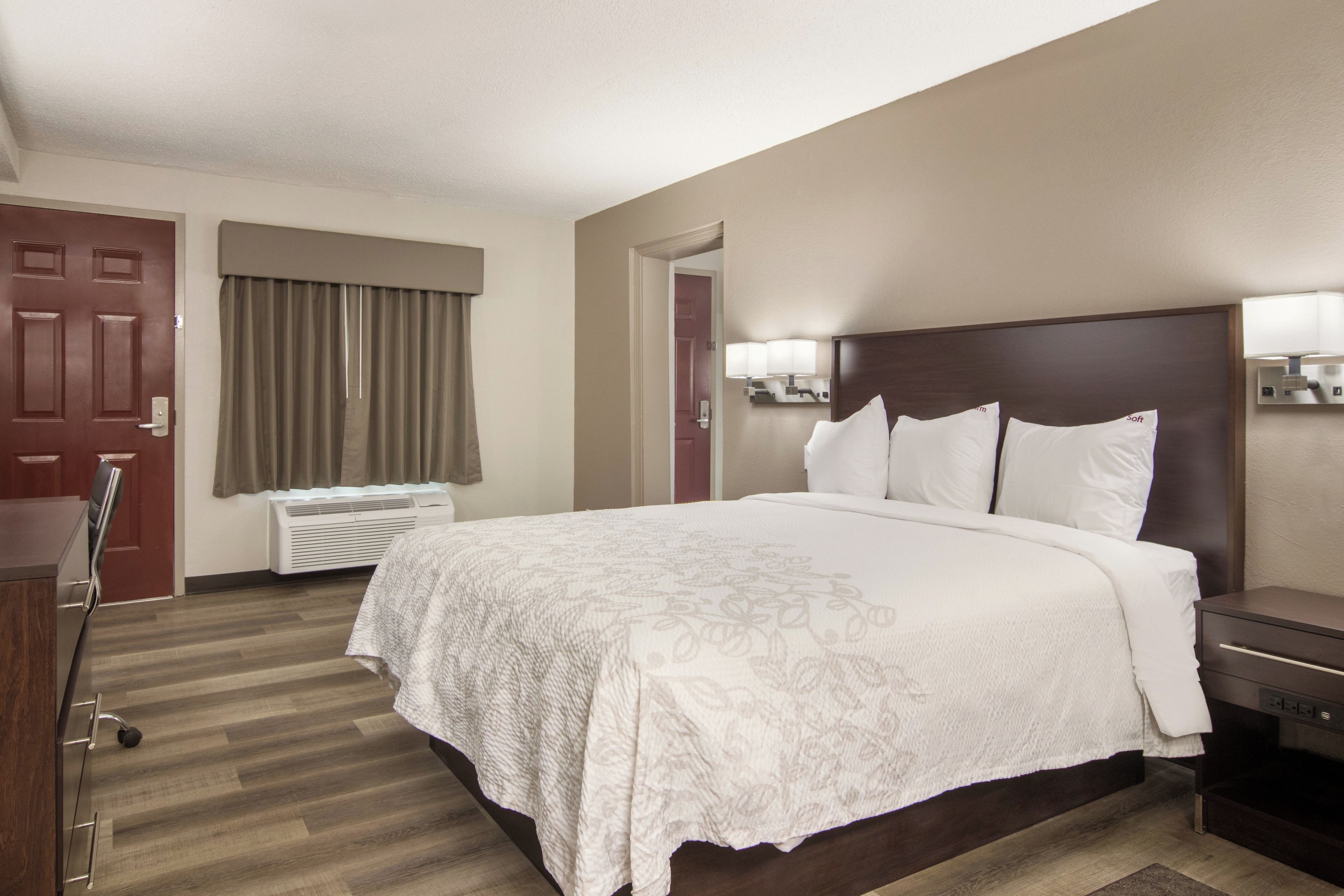 Una habitación de hotel con una cama grande, un escritorio, una silla, un armario y la puerta del baño.