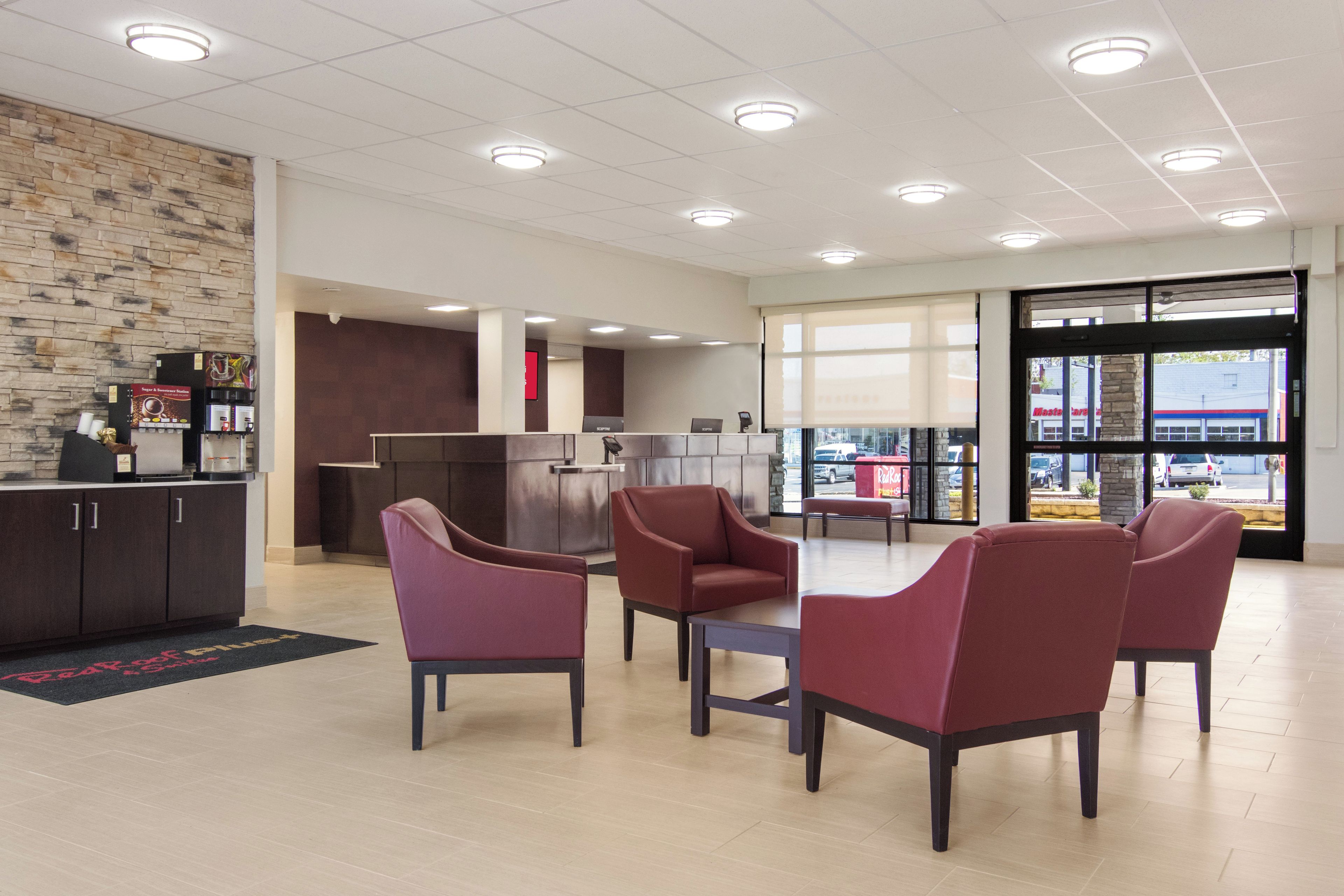 A spacious lobby with a modern design, featuring a reception desk, seating area, and large windows offering a view of the outside.
