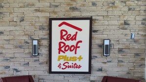 A framed sign with the text "Red Roof Plus Suites" against a stone wall, with two red leather chairs and a small table in front. - Red Roof Inn PLUS+ & Suites Erie (Erie)