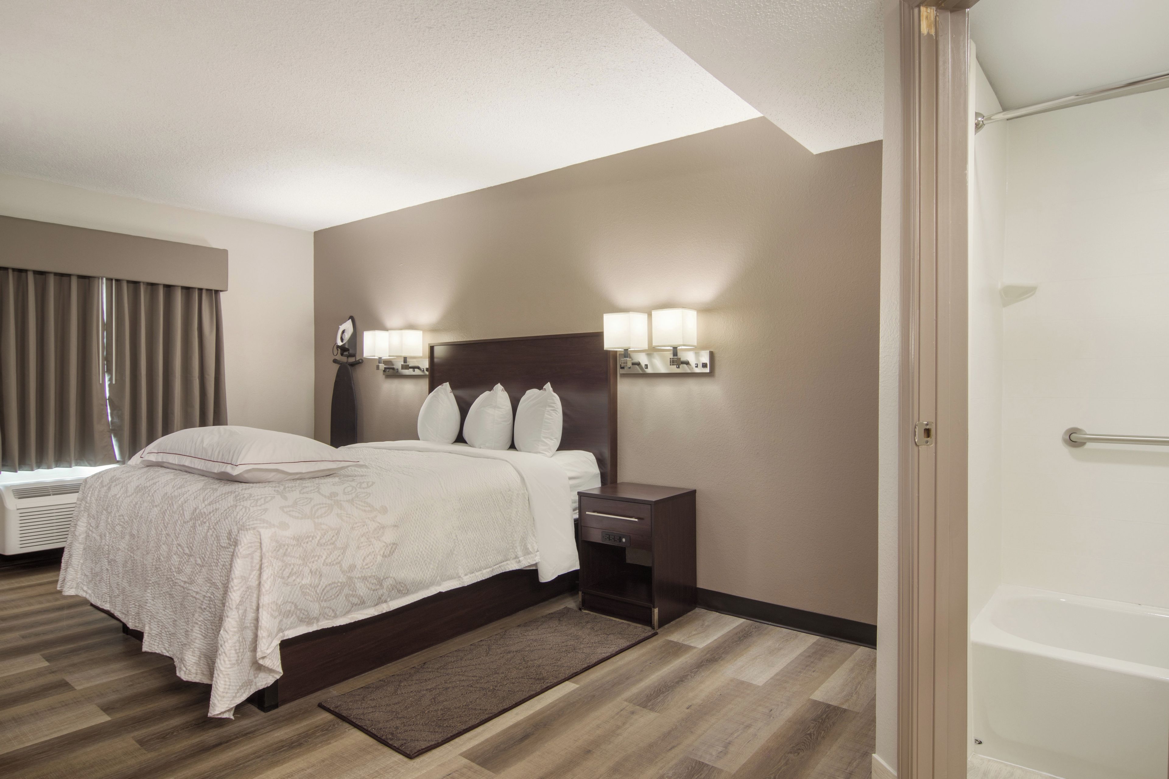 A hotel room with a bed, bedside table, lamp, and a view of the bathroom.