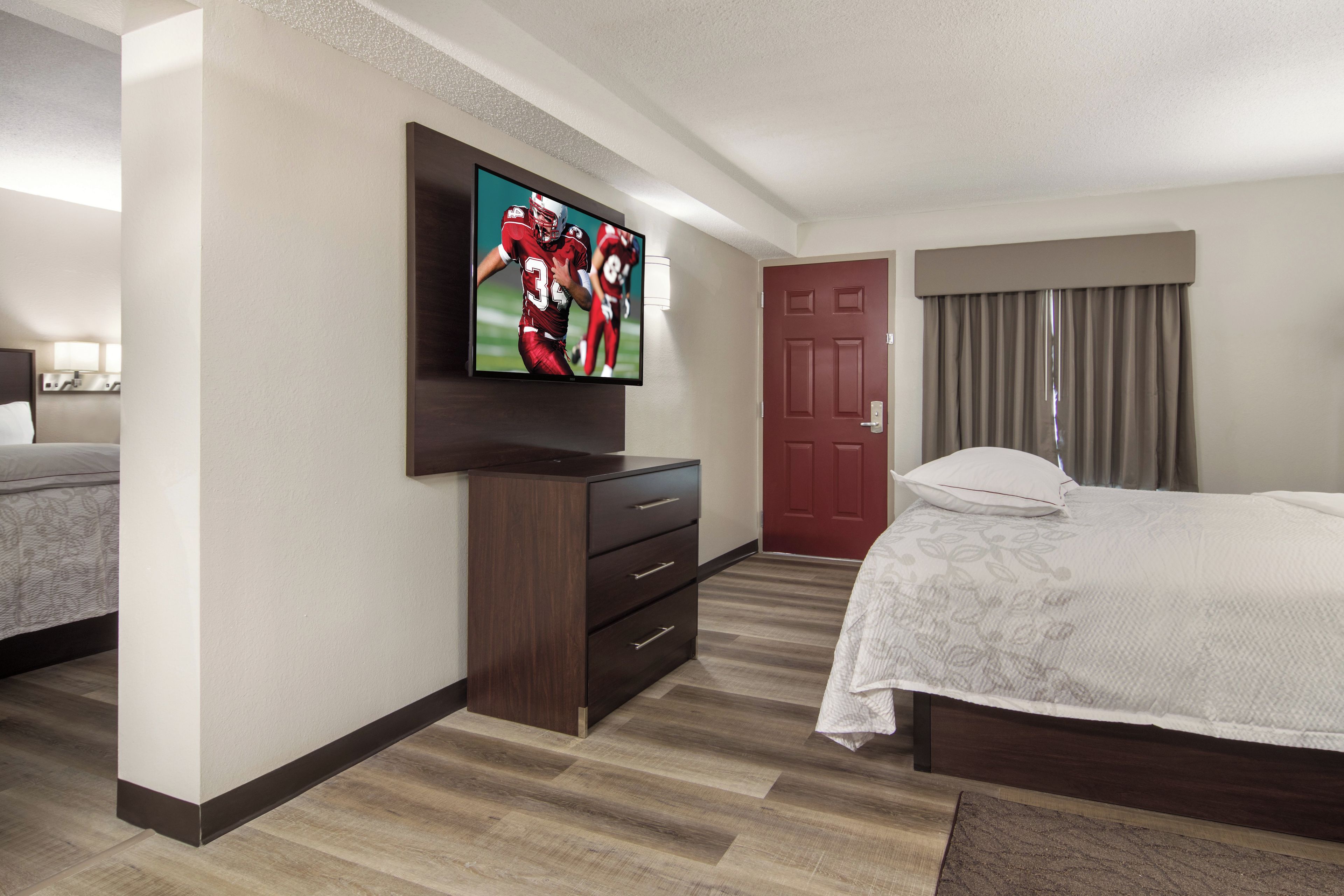 Une chambre d’hôtel avec un lit, un téléviseur fixé au mur, une commode et une porte.