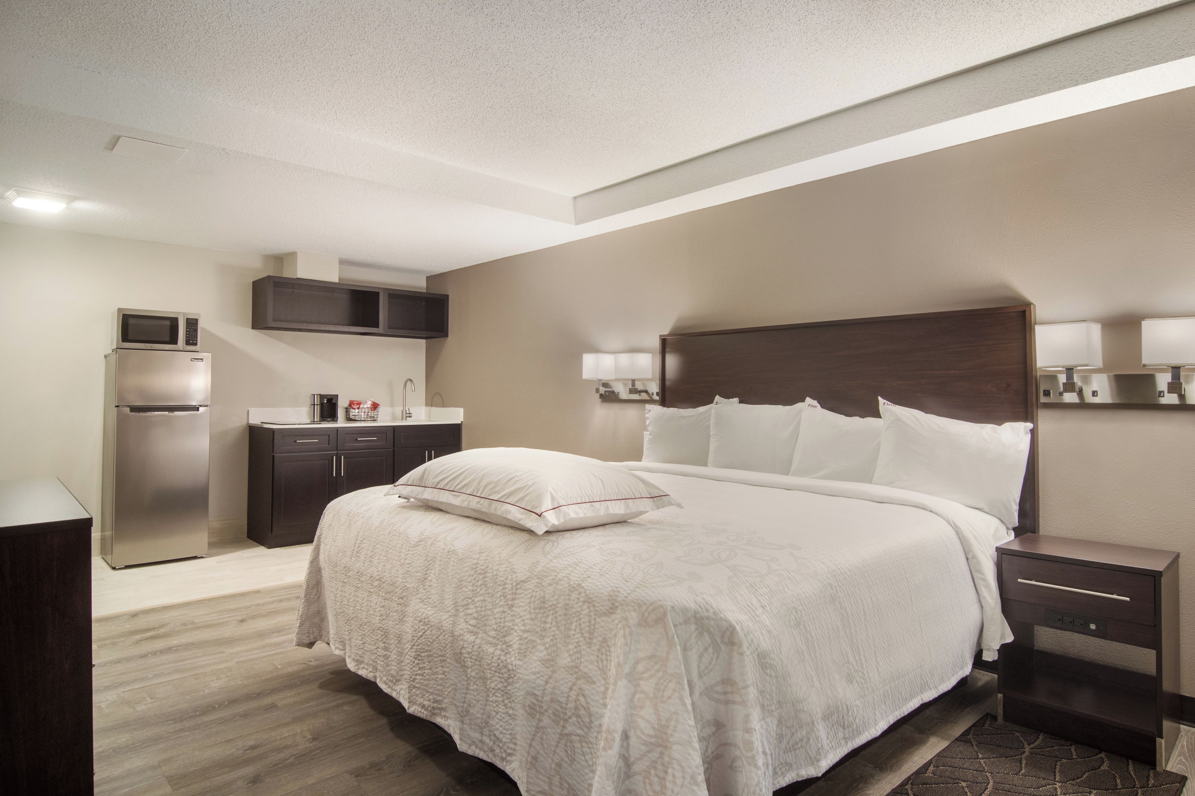 A hotel room with a bed, bedside tables, a desk, a microwave, and a refrigerator.