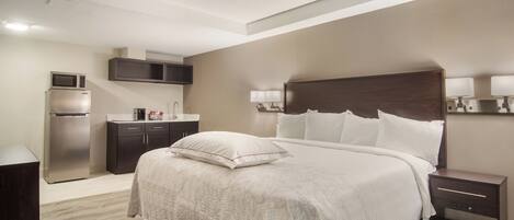 A hotel room with a bed, bedside tables, a desk, a microwave, and a refrigerator.