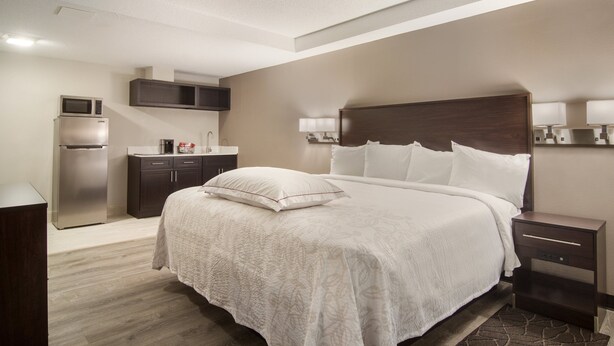 A modern hotel room with a large bed, a built-in microwave, a refrigerator, a small kitchenette, and a bedside table with a lamp. - Red Roof Inn PLUS+ & Suites Erie (Erie)