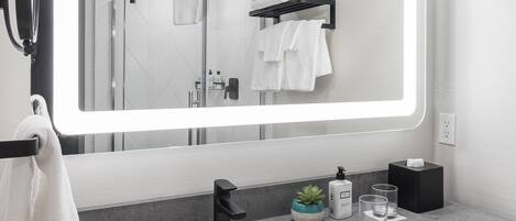 A modern bathroom with a large mirror, a sink, a towel rack, and a small potted plant.
