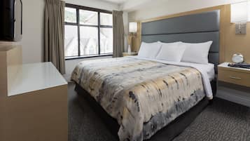 Habitación de hotel con una cama grande, un televisor de pantalla plana, una mesita de noche con lámpara y una ventana con cortinas.