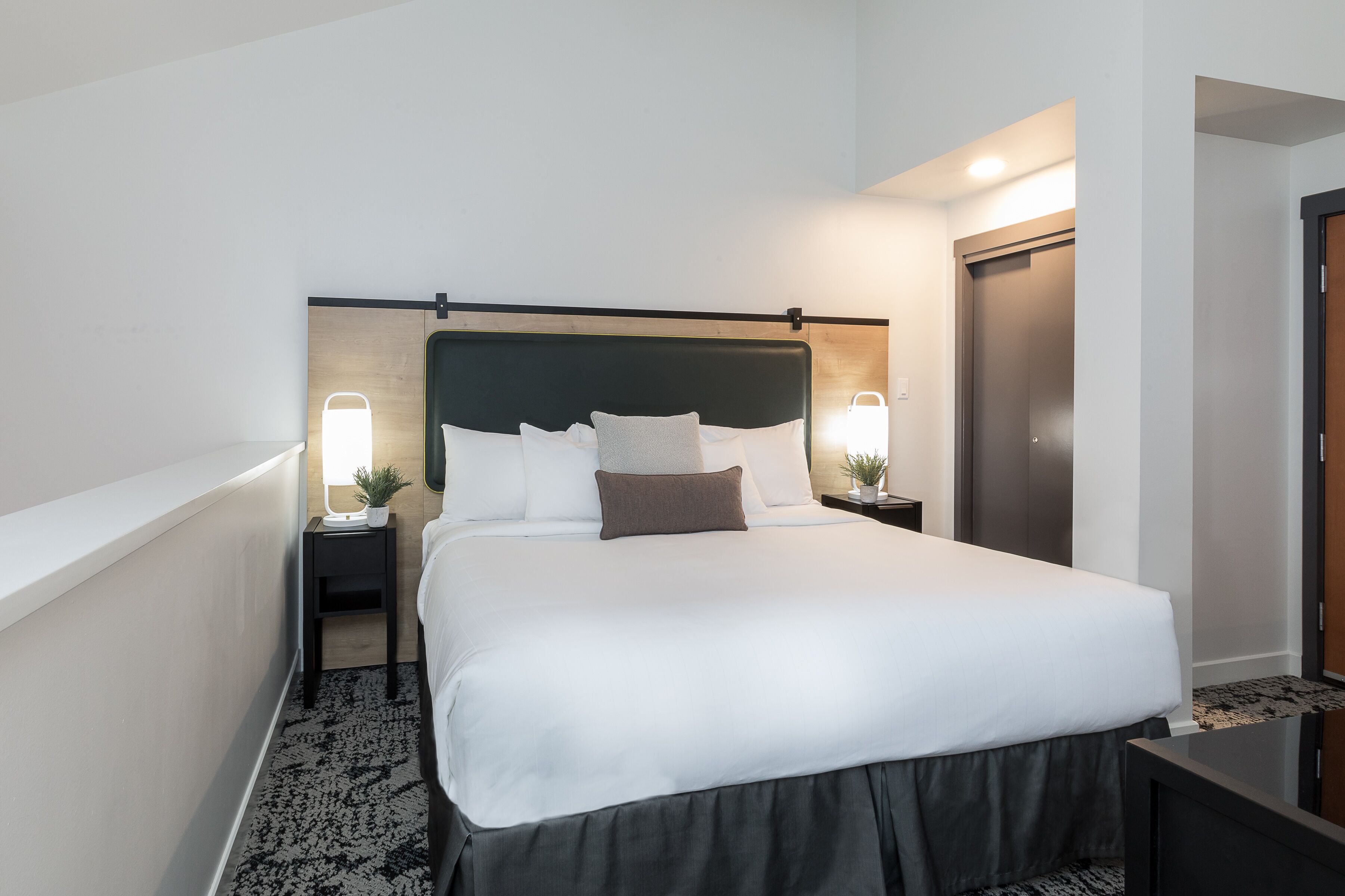 A neatly made bed with white linens and a dark headboard, two bedside tables with lamps, and a wooden floor.