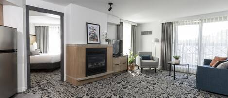 A modern hotel room with a fireplace, a bed, a sofa, and a dining area.