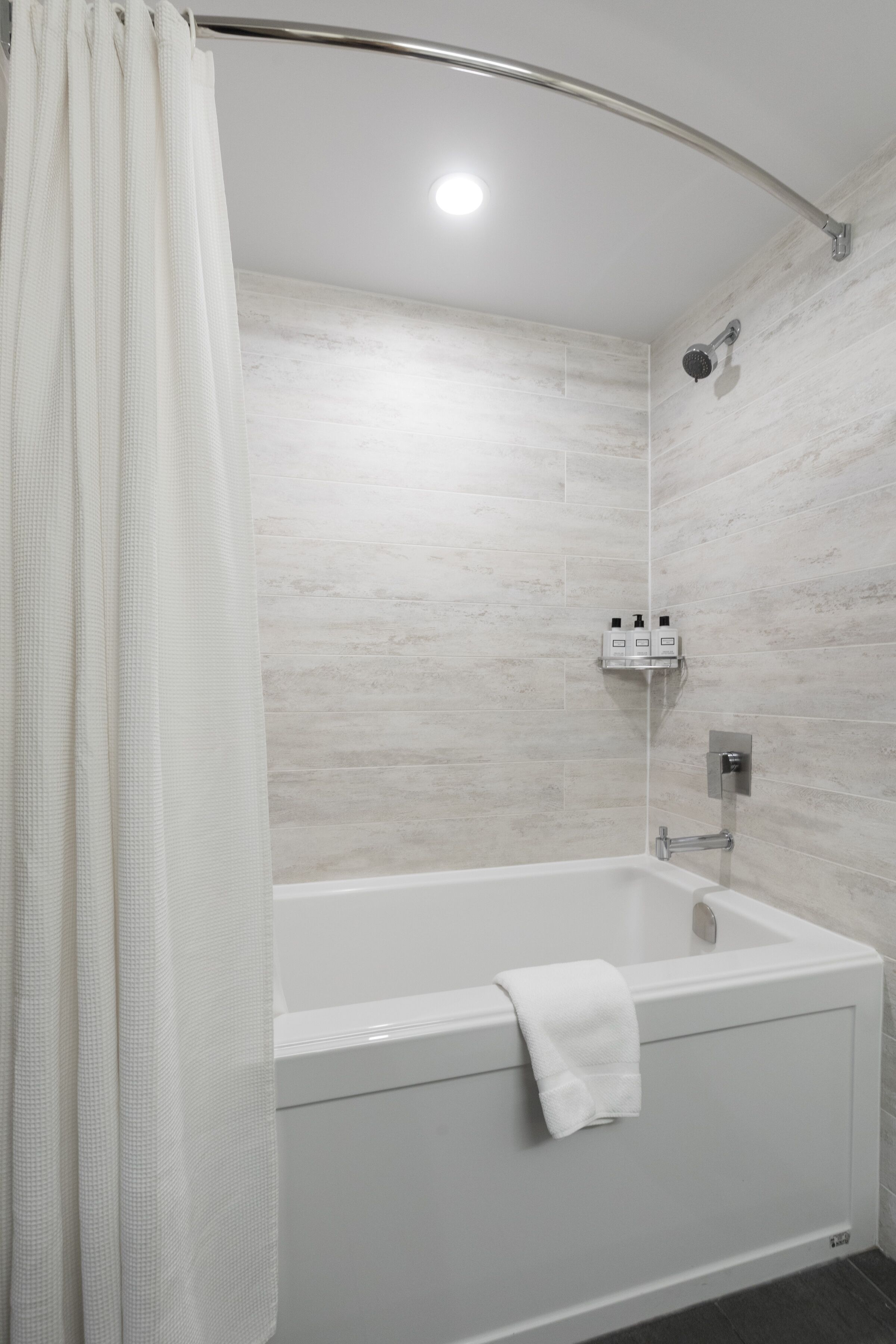 A modern bathroom with a white bathtub, a showerhead, and a towel hanging on the tub.