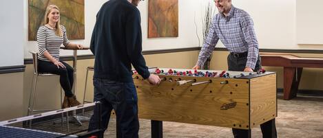 A room with a foosball table, a ping pong table, and two people playing.