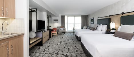 A hotel room with two beds, a desk, a TV, a minibar, and a bathroom.