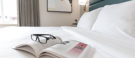 Una cama bien hecha con sábanas blancas, un par de gafas y una revista abierta sobre la cama.