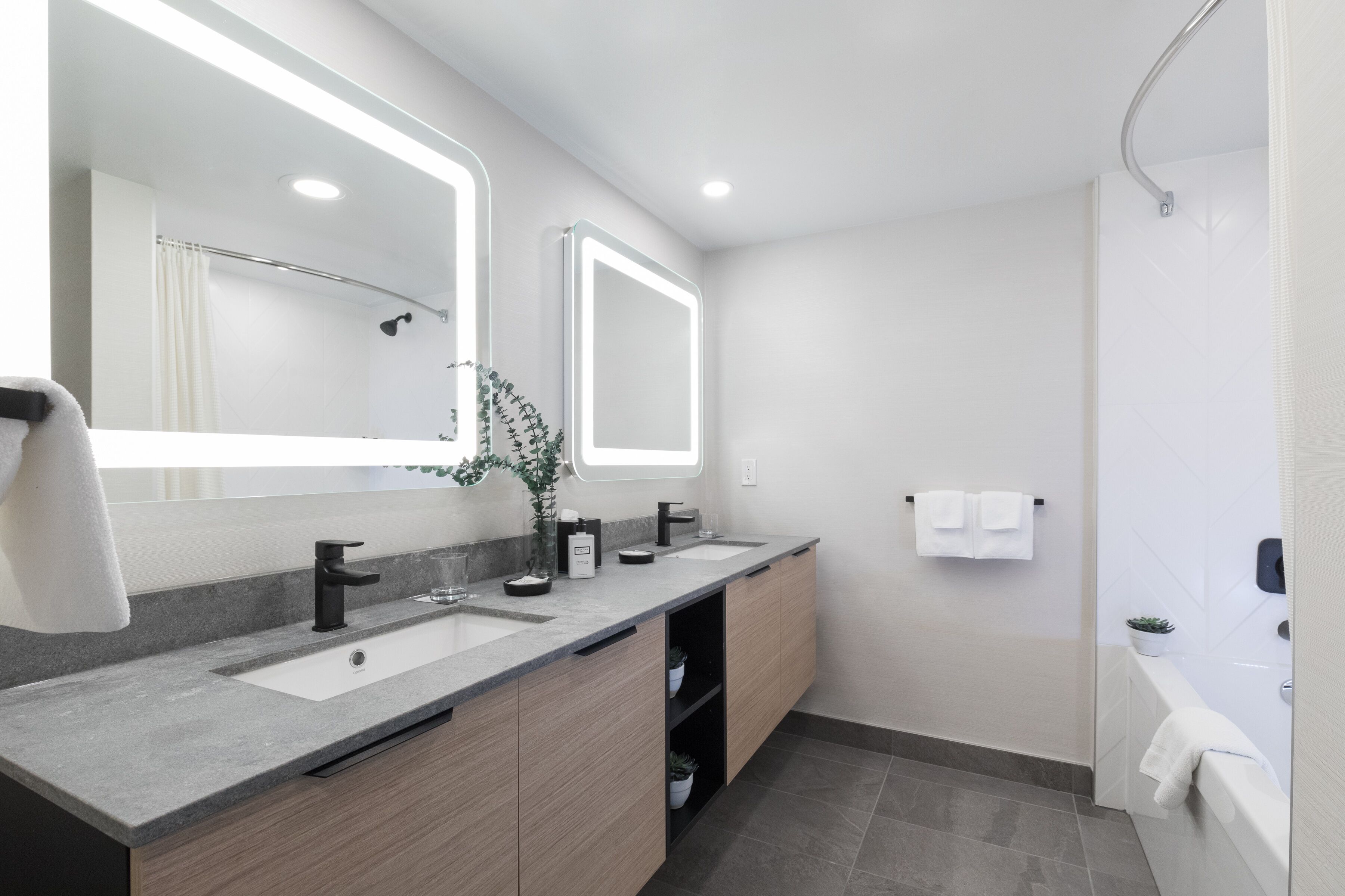 A modern bathroom with two sinks, a large mirror, and a shower area.