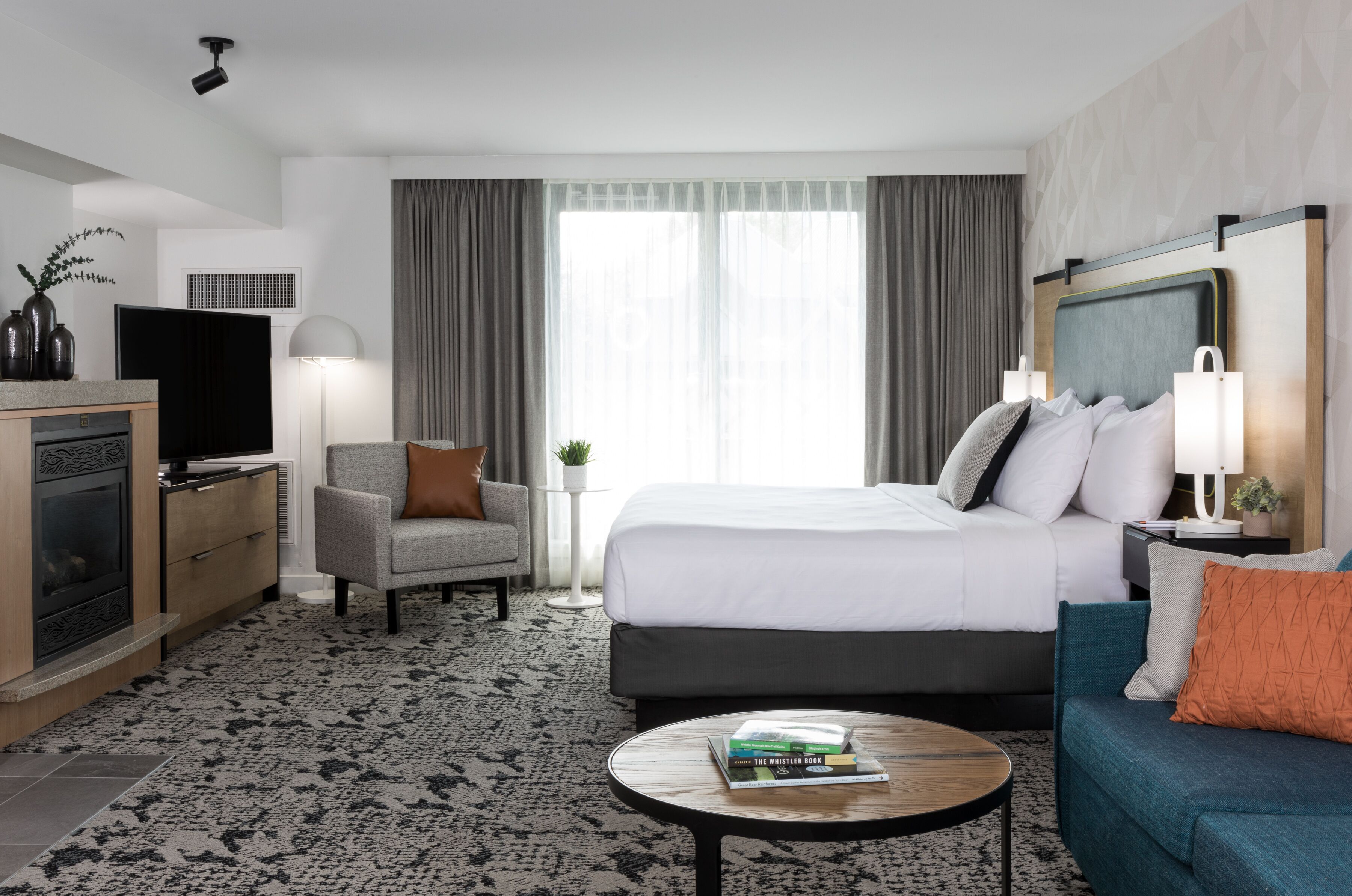A hotel room with a bed, a sofa, a coffee table, a TV, a fireplace, and a window with curtains.