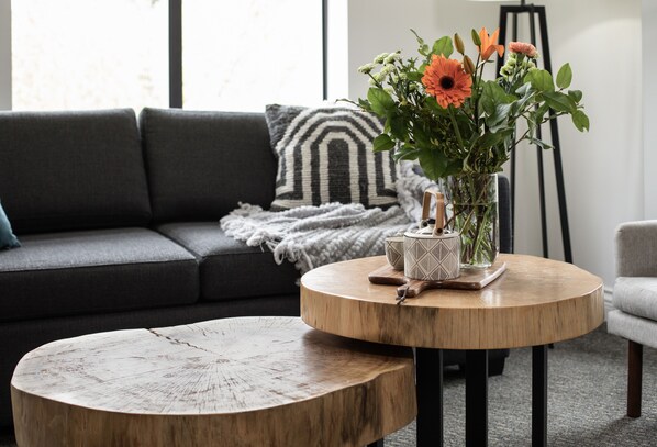 A round wooden coffee table with a vase of flowers on a round wooden table in a living room.