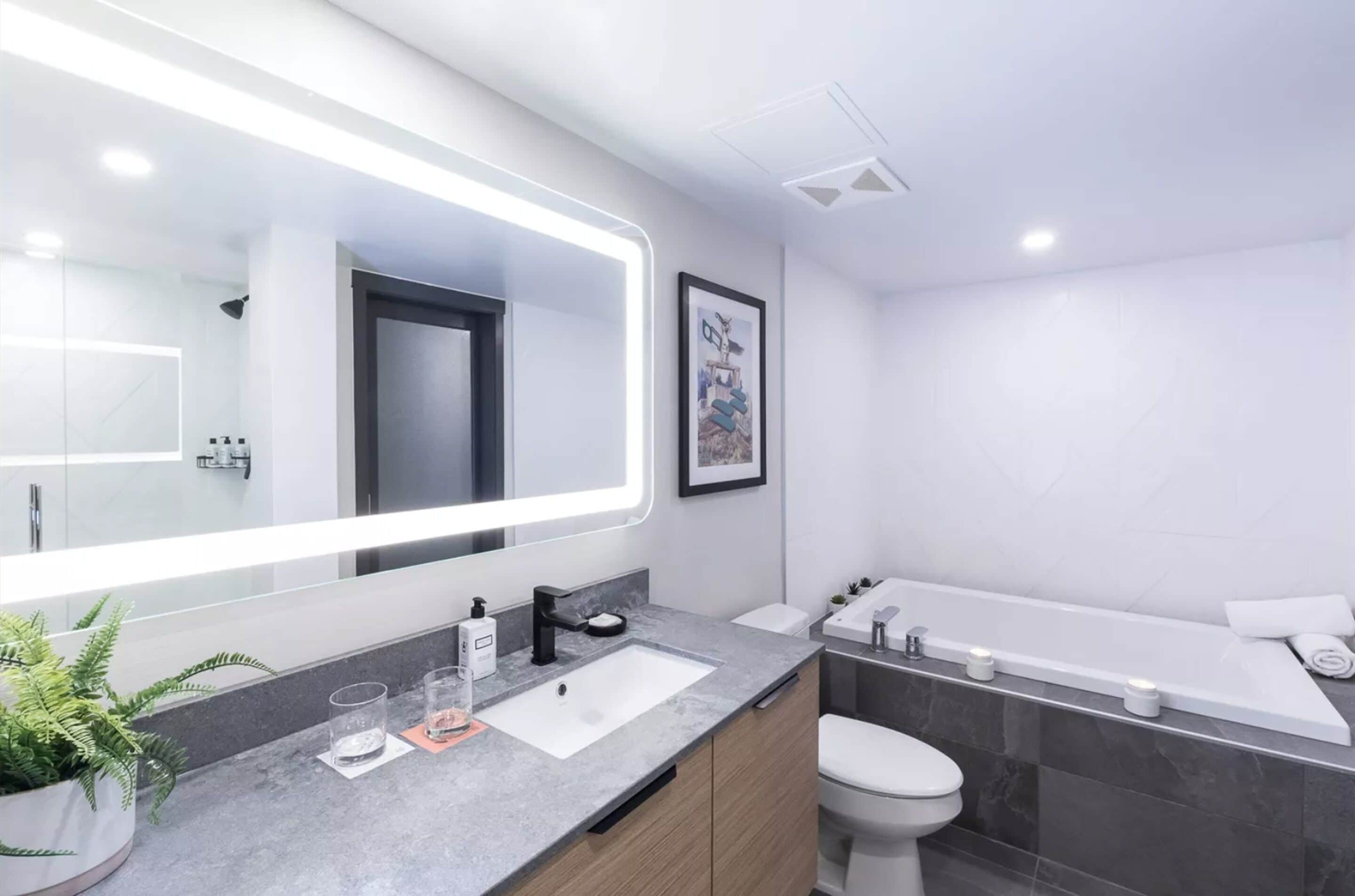 A modern bathroom with a large mirror, a sink, a toilet, and a bathtub.