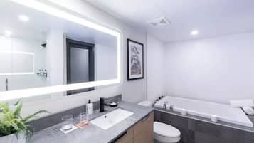 A modern bathroom with a large mirror, a sink, a toilet, and a bathtub.