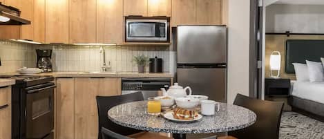 Une cuisine moderne avec des meubles en bois, un four à micro-ondes, un réfrigérateur et un coin repas comprenant une table ronde et des chaises.