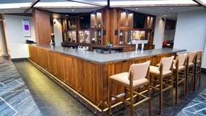 Un bar moderno con mostrador de madera, varias opciones de asiento y suelo con diseño hexagonal.